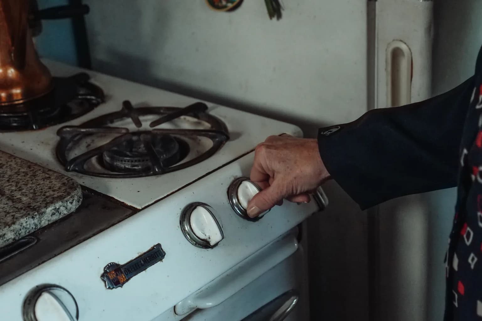 An older hand turning the control knob of a well-used white gas range